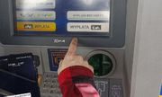 Zdjęcie przedstawia dłoń sięgającą do klawiatury bankomatu na ekranie którego wyświetla się kilka komunikatów.