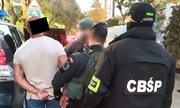 funkcjonariusz CBŚP i funkcjonariusze CBŚP, Guardia Civil z zatrzymanym mężczyzną zakutym w kajdanki przy radiowozie