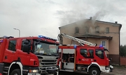Pożar domu wielorodzinnego, przed budynkiem stoją dwa wozy strażackie