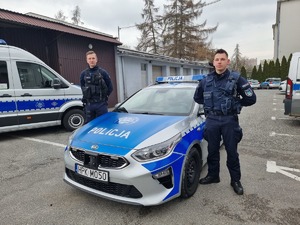 dwaj umundurowani policjanci stoją po obu stronach radiowozu