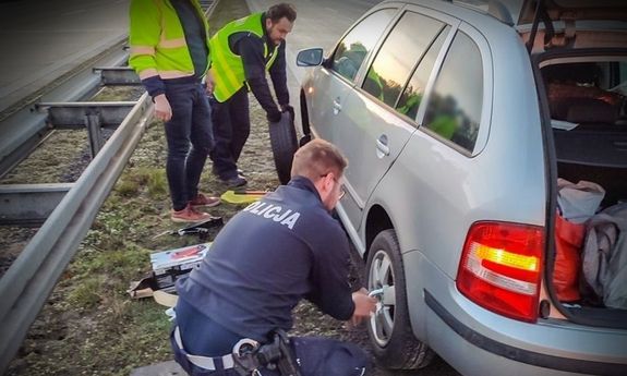 umundurowany policjant w trakcie zmiany koła