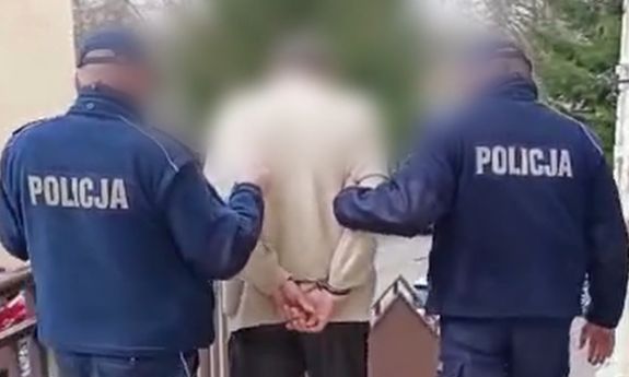 Zdjęcie przedstawia dwóch umundurowanych policjantów, którzy prowadzą pomiędzy sobą zatrzymanego mężczyznę.