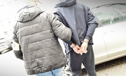 policjant prowadzi zatrzymanego mężczyznę w kajdankach
