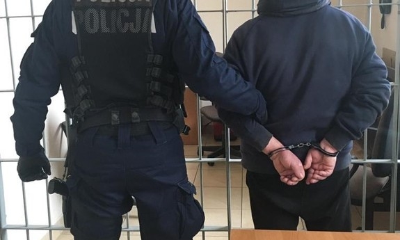 policjant prowadzi zatrzymanego mężczyznę w kajdankach