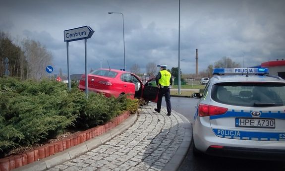 policjant wydziału ruchu drogowego, radiowóz oraz auto osobowe koloru czerwonego na środku ronda