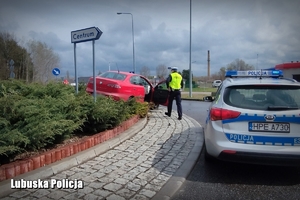 policjant wydziału ruchu drogowego, radiowóz oraz auto osobowe koloru czerwonego na środku ronda