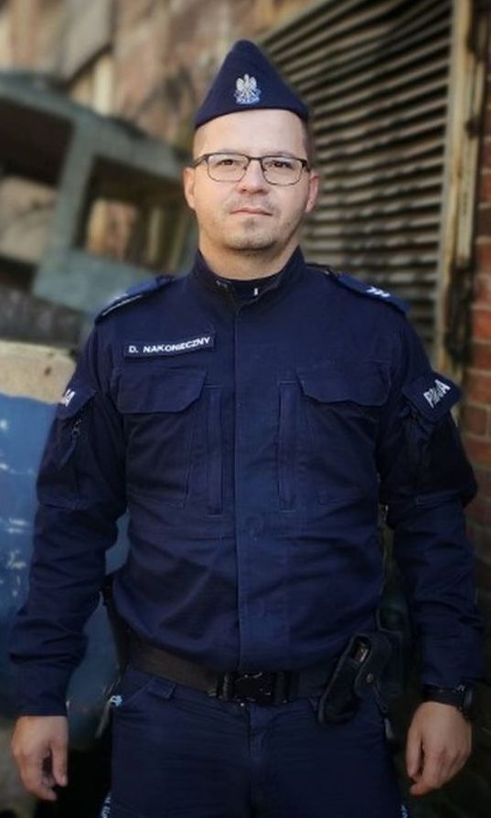 Zdjęcie przedstawi umundurowanego policjanta, który pozuje do zdjęcia.