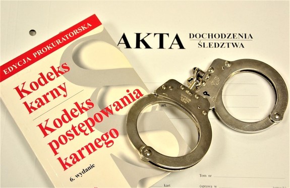 okładka akt na niej kodeks karny i postępowania karnego obok kajdanki