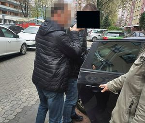 Nieumundurowany policjant wprowadza zatrzymanego mężczyznę do samochodu