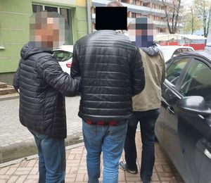 Dwaj nieumundurowani policjanci prowadza zatrzymanego mężczyznę