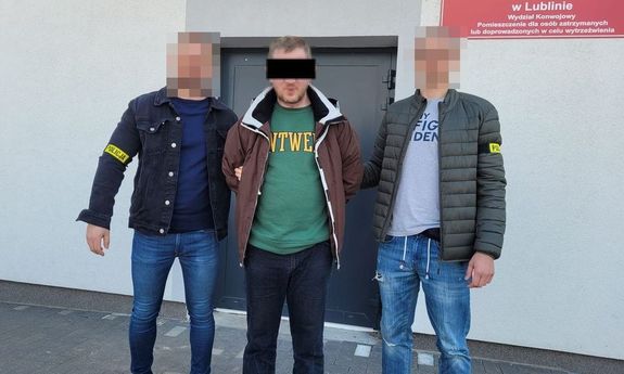 Zdjęcie przedstawia dwóch nieumundurowanych policjantów, którzy prowadzą pomiędzy sobą zatrzymanego. Twarz mężczyzny zasłania czarny prostokąt.