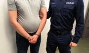 Na zdjęciu policjant z zatrzymanym mężczyzną w kajdankach na rękach