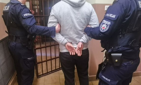 policjanci prowadzą zatrzymaną osobę, która ma na rękach kajdanki