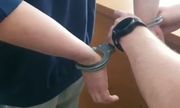 policjant zakłada zatrzymanemu kajdanki na ręce trzymane z tyłu