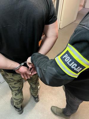 Napis Policja na opasce na ramieniu policjanta i zatrzymany mężczyzna w kajdankach