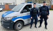 dwaj umundurowani policjanci stoją przy policyjnym furgonie
