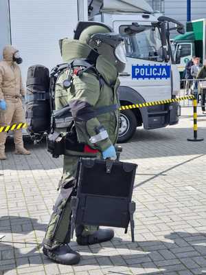 mężczyzna w specjalnym kombinezonie ze specjalistycznym sprzętem zmierza do plecaka, który stoi przy aucie