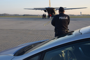 Policjant przy radiowozie obserwujący załadunek organu do transplantacji do samolotu Casa.