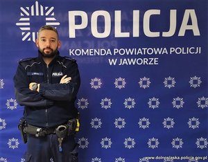 Umundurowany policjant na tle ścianki z napisem Komenda Powiatowa Policji w Jaworze