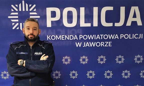 Umundurowany policjant na tle ścianki z napisem Komenda Powiatowa Policji w Jaworze