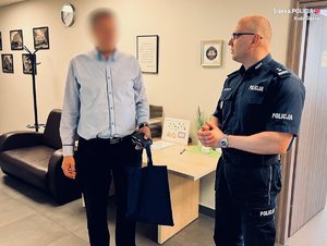 zdjęcie ze spotkania - policjant i mężczyzna na korytarzu przy biurze, na ścianie widoczne zdjęcia i logo policji