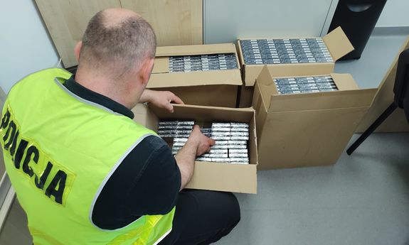 policjant trzyma w ręku kilka paczek papierosów