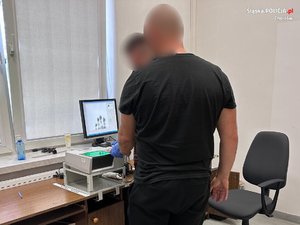 Zdjęcie przedstawia zatrzymanego podczas pobierania odcisków palców