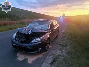 Na zdjęciu zgnieciona maska samochodu osobowego w wypadku drogowym. w dali odblaski sygnałów policji