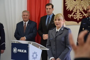 umundurowana policjantka stoi przy mównicy a z tyłu widać dwóch mężczyzn w garniturach