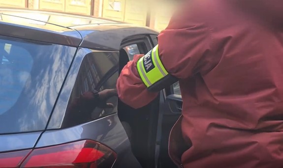zatrzymany wsiada do policyjnego auta - obok widać towarzyszącego mu policjanta