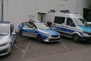policjant i policjantka stojący przy radiowozie, obok widać inne zaparkowane radiowozy
