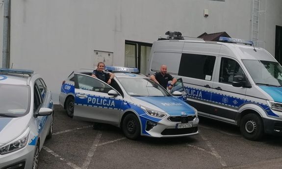 policjant i policjantka stojący przy radiowozie, obok widać inne zaparkowane radiowozy