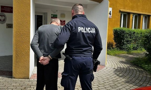 umundurowany policjant z zatrzymanym mężczyzną przed budynkiem Prokuratury