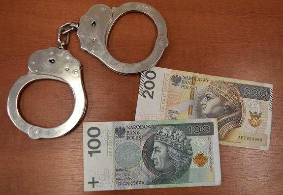 dwa banknoty stu i dwustuzłotowe leżą na stole, a obok kajdanki