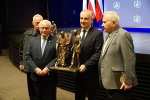 czterej mężczyźni w garniturach stoją przed scena i trzymają statuetki Jana Pawła II i Ronalda Regana