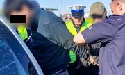 Zatrzymany mężczyzna ma zapinane kajdanki na ręce przez policjantów
