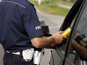 policjant z alkomatem stoi przy zaparkowanym obok samochodzie i wystawia urządzenie w kierunku kierującego, który ma otwartą szybę.