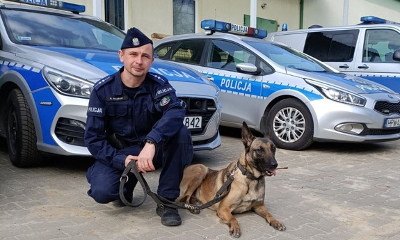 policjant z psem służbowym, w tle radiowozy policyjne