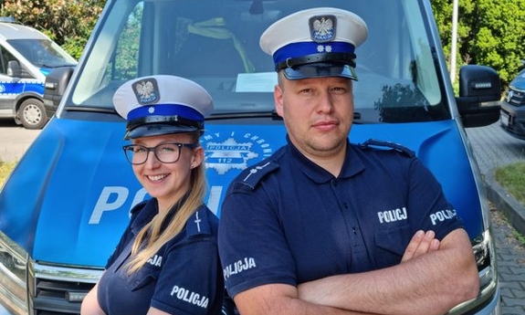 policjant i policjantka stoją przed radiowozem policyjnym