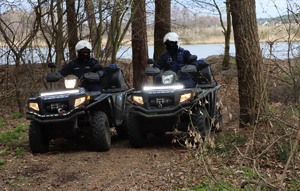 dwaj policjanci na quadach w zalesionym terenie, w tle zbiornik wodny