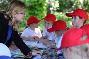 grupa małych dzieci przy stoisku z gazetami, kobieta rozmawia z jednym z nich