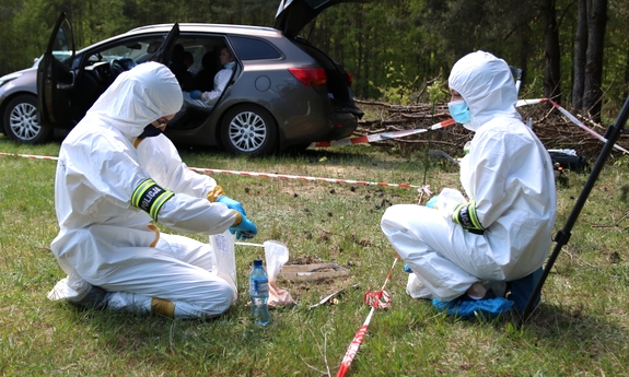 Policjanci Laboratorium Kryminalistycznego ubrani w białe kombinezony zbierają ślady