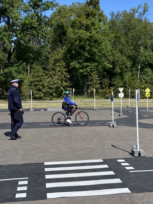 uczestnik turnieju na rowerze w trakcie pokonywania toru przeszkód, policjant obserwuje poprawność ich pokonywania