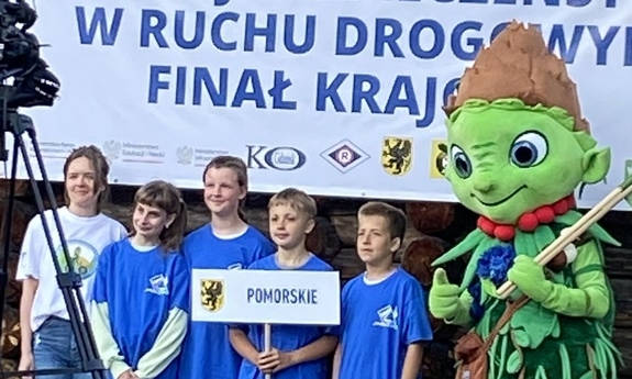 grupa dzieci stoi na scenie, jedno z nich trzyma plakietkę z napisem pomorskie, obok dzieci stoi kolorowa maskotka