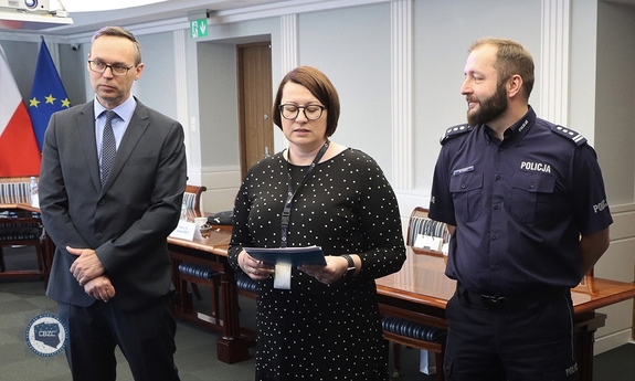 na sali od lewej strony stoi mężczyzna, kobieta i policjant