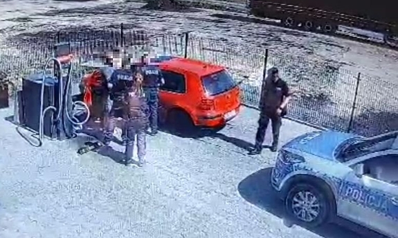 zdjęcie z monitoringu przedstawia policjantów w trakcie zatrzymania mężczyzny przy samochodzie