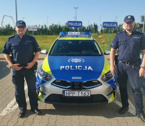 dwaj policjanci stoją przed radiowozem policyjnym