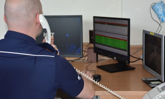 Policjant - oficer dyżurny odbiera telefon w czasie pełnienia służby - widok z tyłu