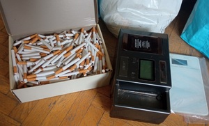 pudełko z luźno ułożonymi papierosami, przy nim dwie maszynki do papierosów