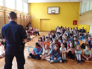 Policjant z grupą dzieci i ich opiekunami, w sali gimnastycznej.